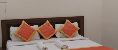 A neatly made bed with a wooden headboard, white bedding, and orange accents.