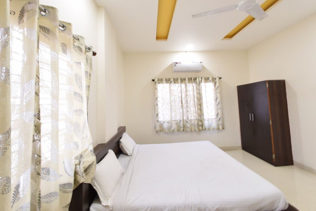 A bedroom with a bed, curtains, a wardrobe, a ceiling fan, and an air conditioning unit.