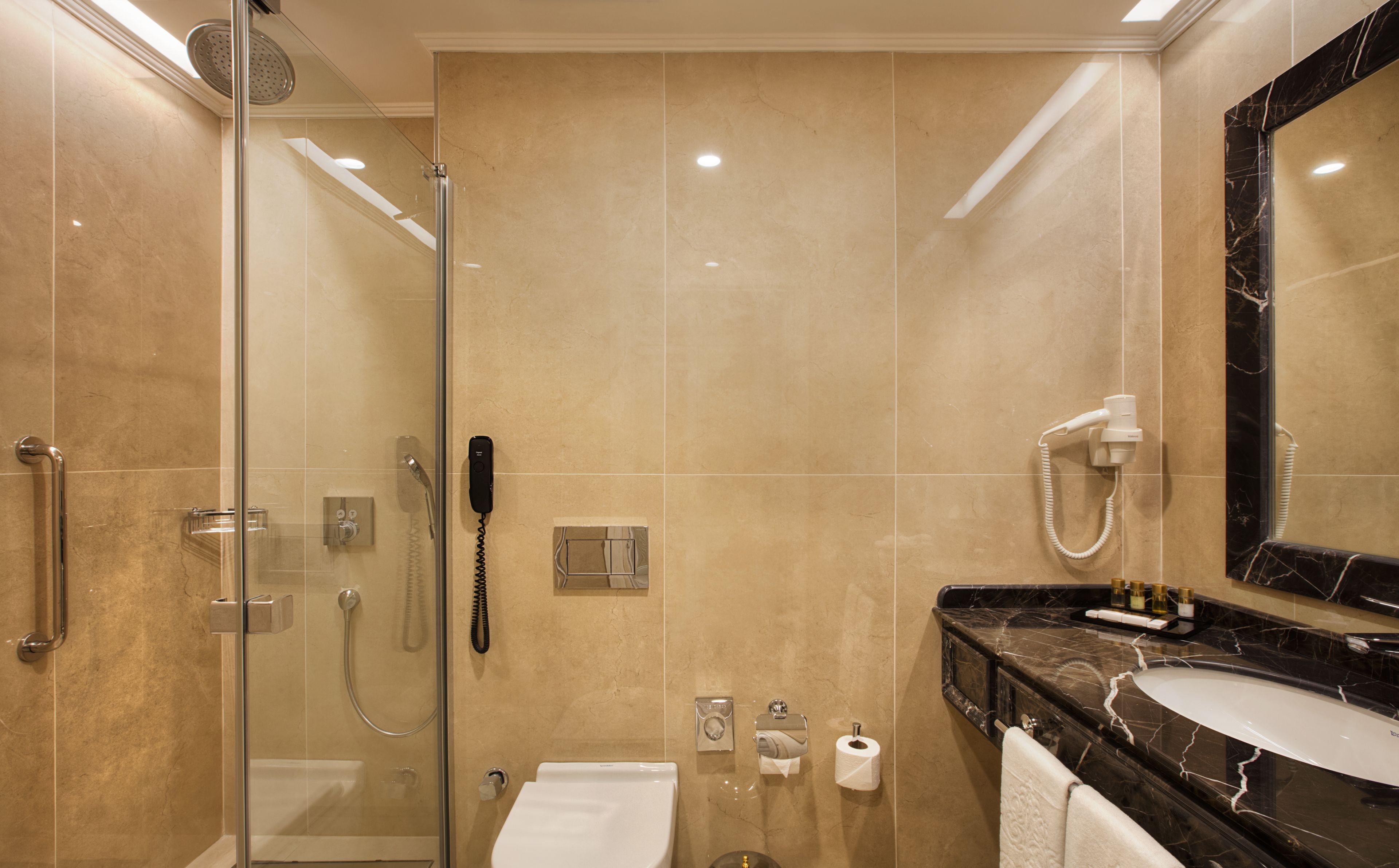 A modern bathroom with a glass-enclosed shower, a marble-tiled wall, a black marble sink, and a large mirror.
