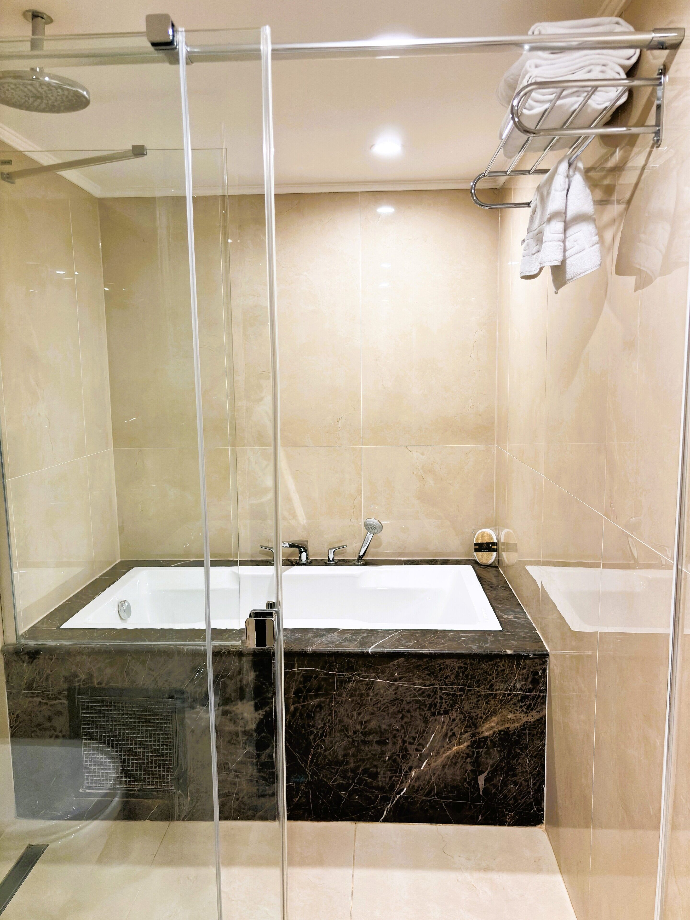 A modern bathroom with a glass-enclosed shower, a large bathtub, and a towel rack.