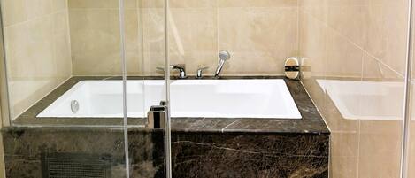 A modern bathroom with a glass-enclosed shower, a large bathtub, and a towel rack.