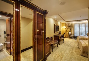 A hotel room with a large mirror, a desk, a chair, a bed, and a bathroom.