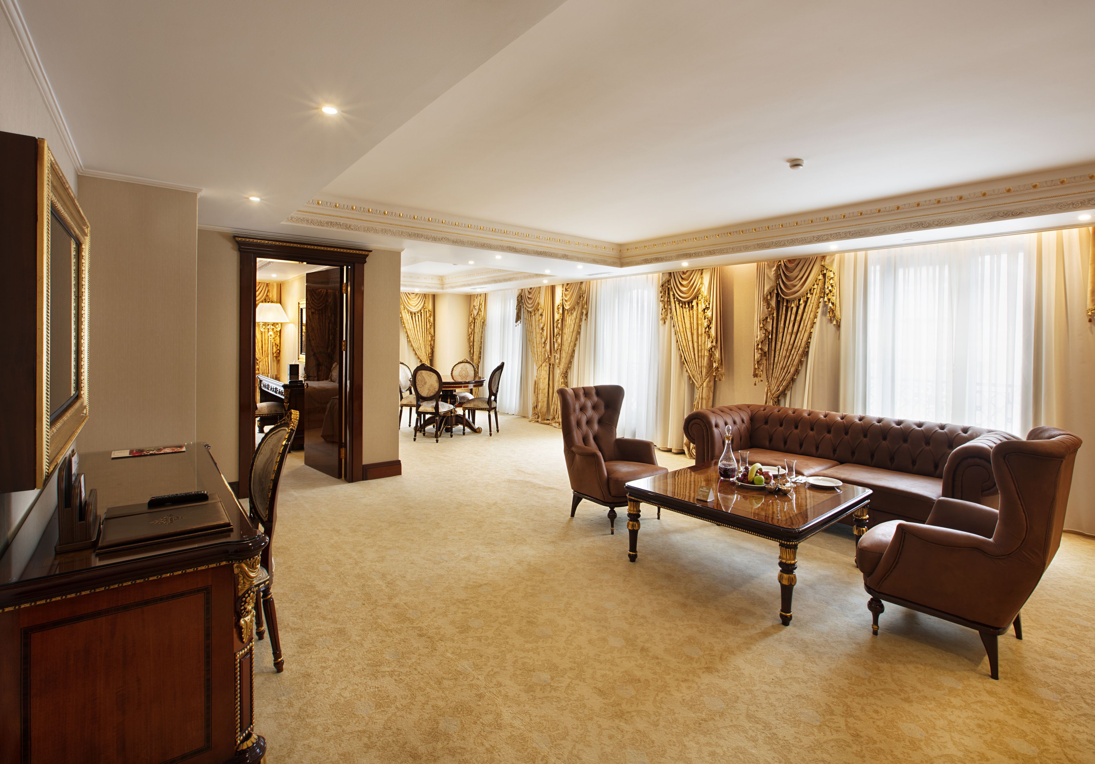 A spacious living room with a large sofa, two armchairs, a coffee table, and a television on a wooden cabinet.
