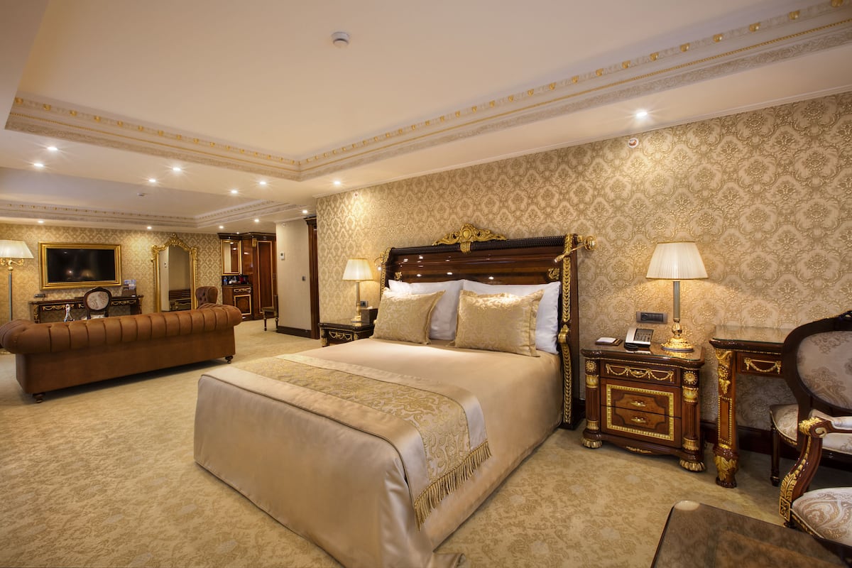 A spacious hotel room with a large bed, a sitting area, and a television.