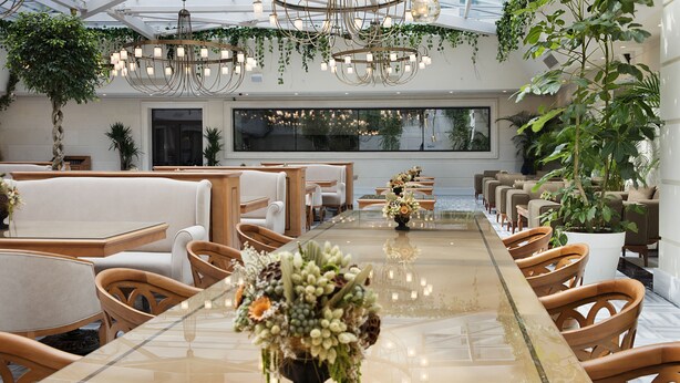 A spacious indoor area with a long table, multiple seating arrangements, and hanging plants. - Ottoman's Life Hotel Deluxe (Istanbul)