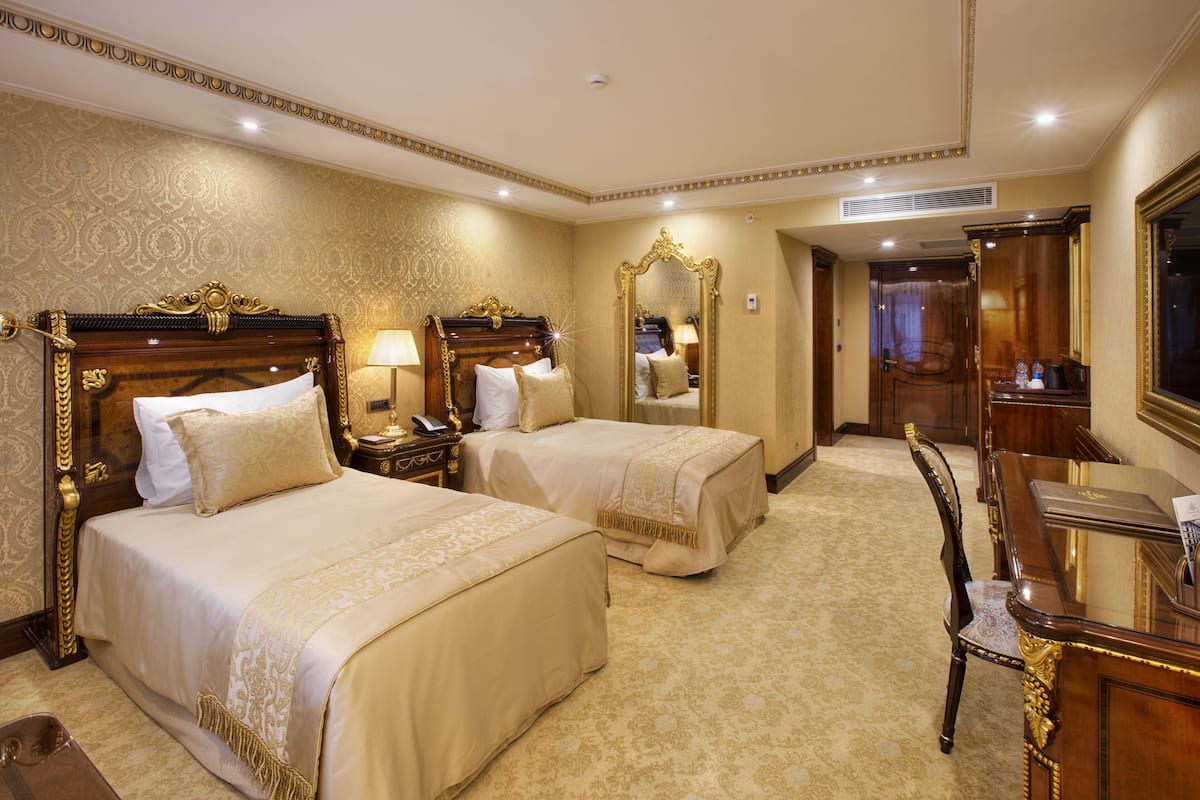 A hotel room with two beds, a desk, a chair, and a large mirror.