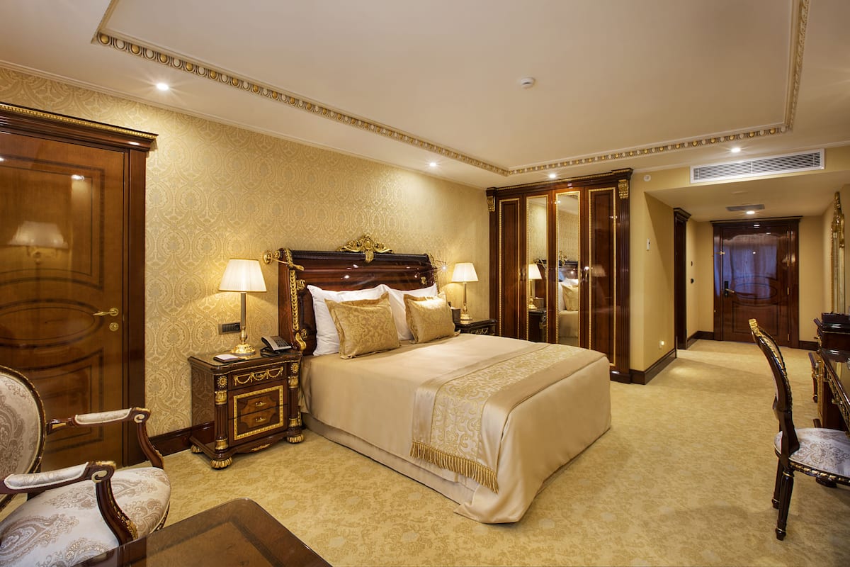 A spacious bedroom with a large bed, two bedside tables with lamps, a wardrobe, and a mirror.