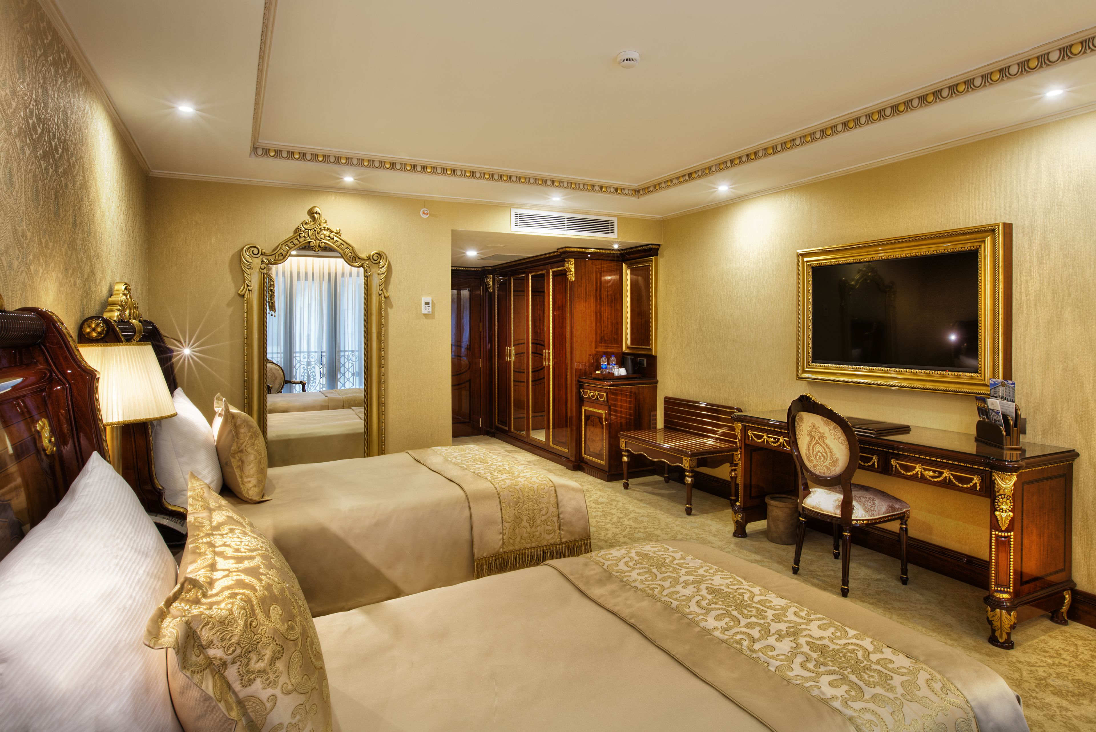 A hotel room with two beds, a desk, a chair, a mirror, and a television.