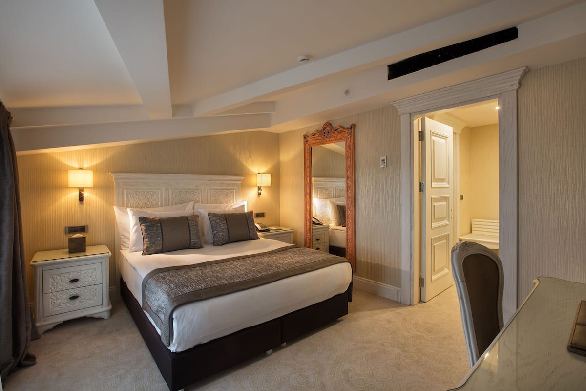 A hotel room with a large bed, bedside tables, a mirror, and a chair.