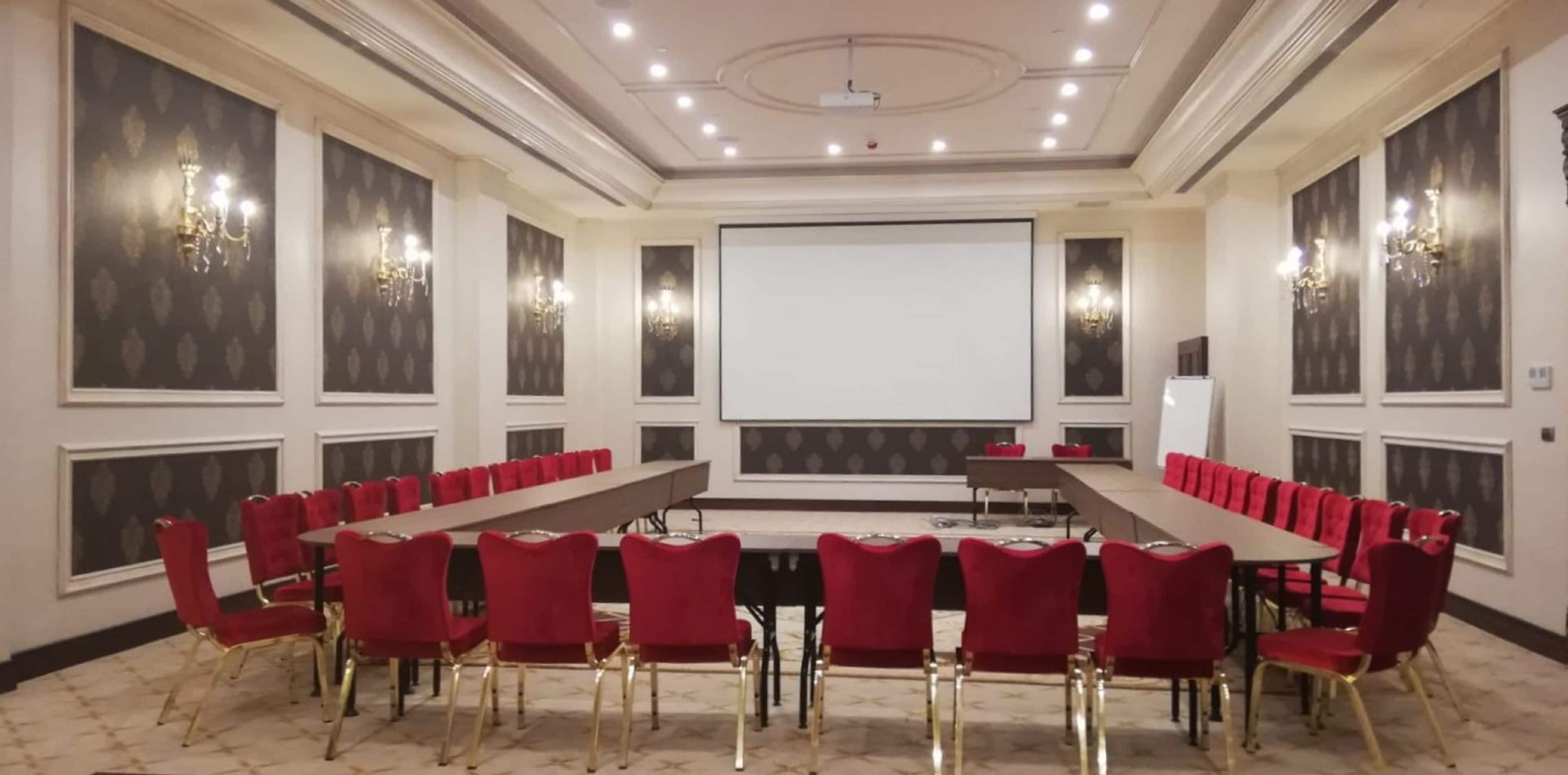 A conference room with a long table, red chairs, and a projector screen.