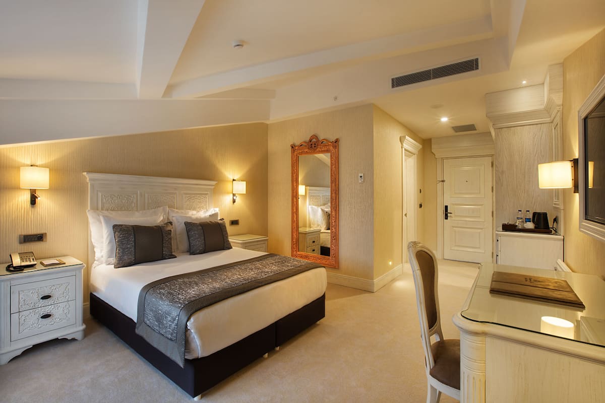 A spacious bedroom with a large bed, bedside tables, a mirror, a desk, and a chair.