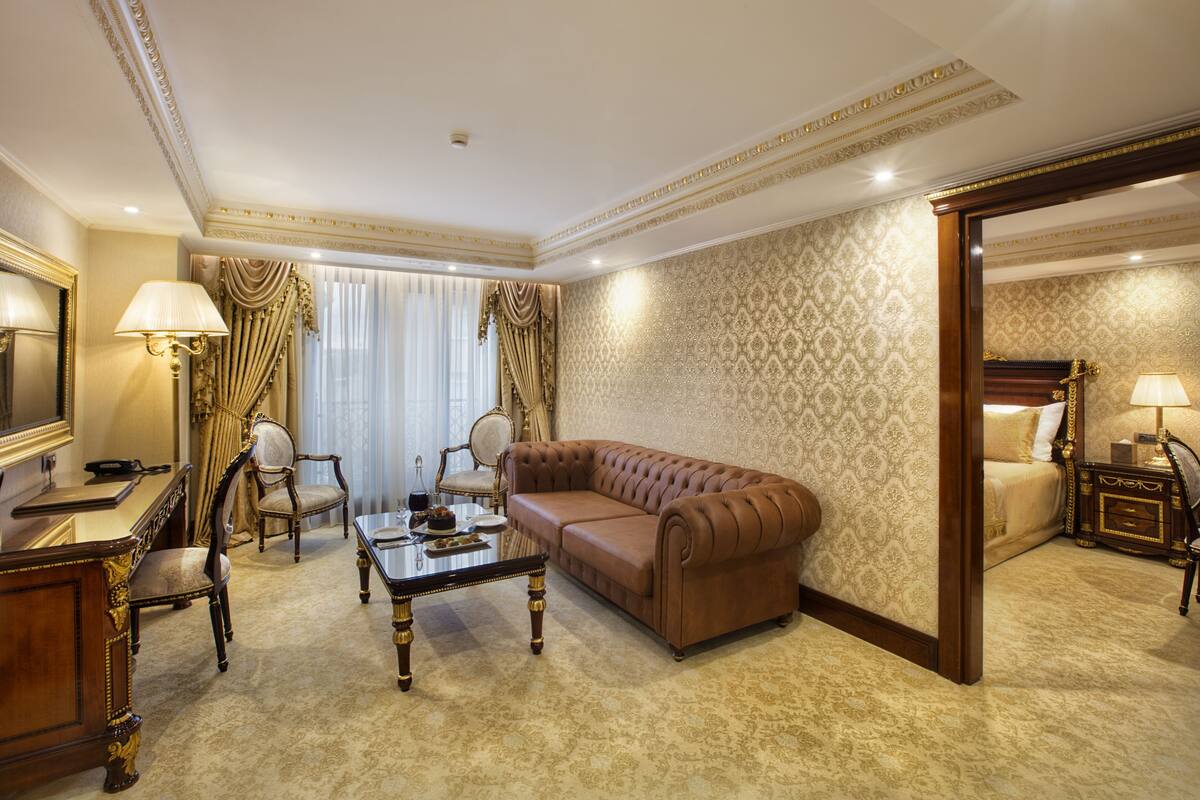 A luxurious living room with a brown sofa, two armchairs, a glass coffee table, and a desk with a lamp.