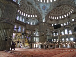 Vista interna di una grande moschea con dettagli architettonici elaborati, numerose arcate e uno spazio centrale aperto con un tappeto decorato.