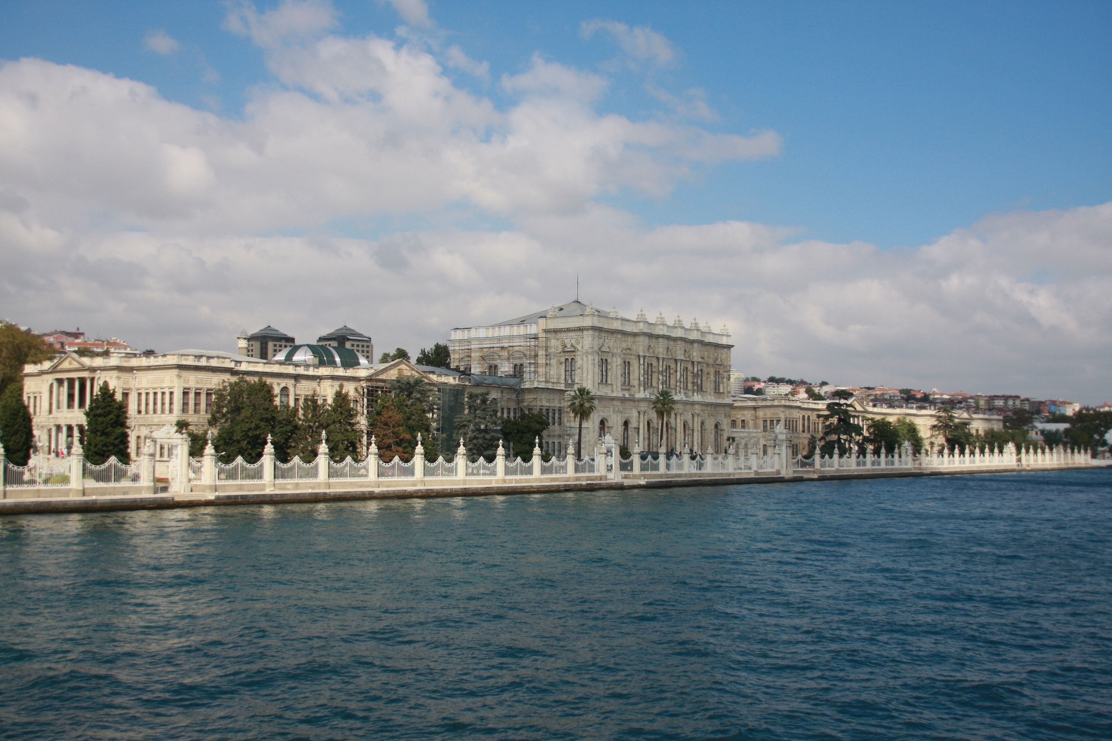 A waterfront building with classical architecture, a large central dome, and a white fence along the water's edge.