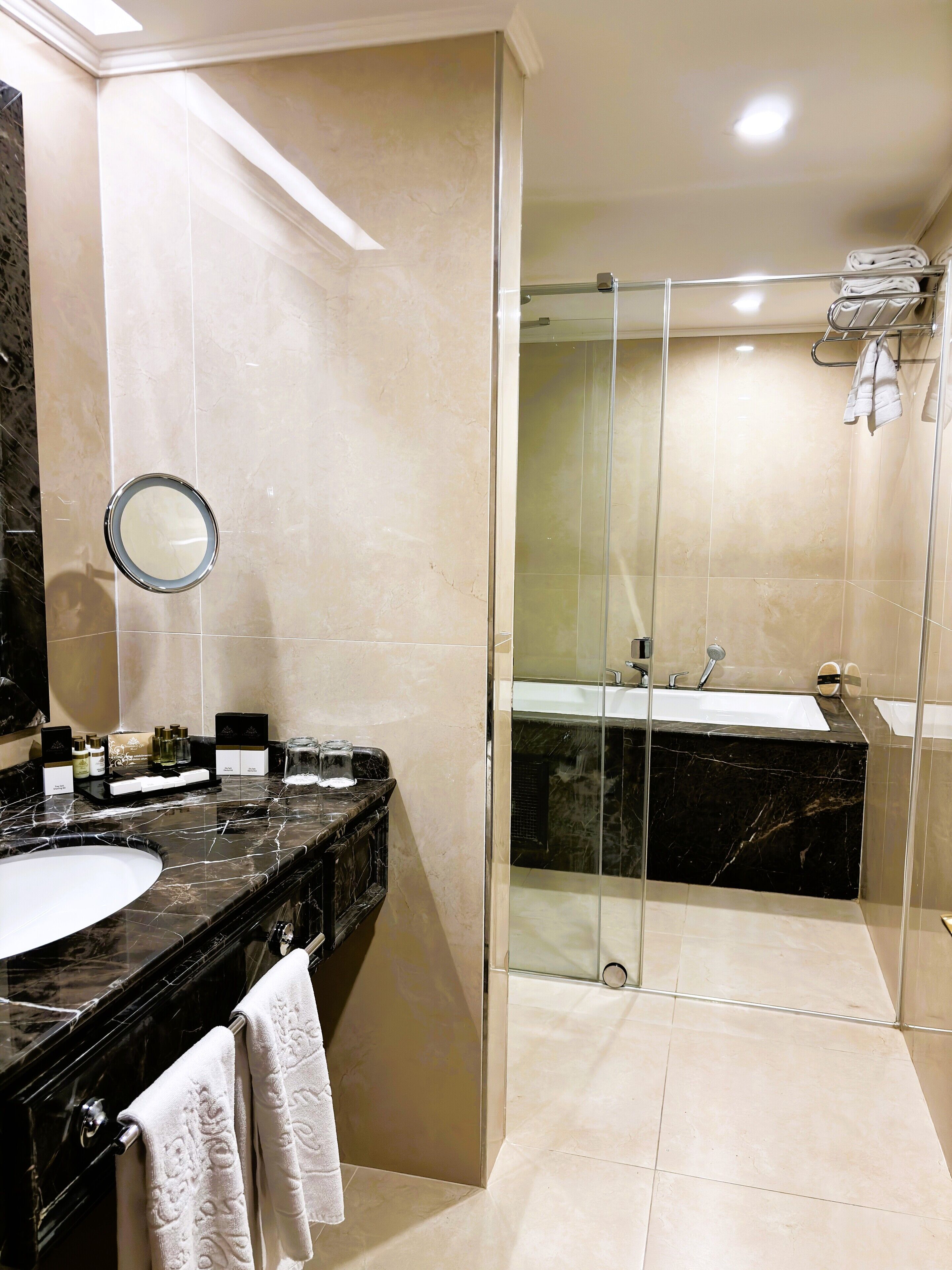 Un baño moderno con lavamanos de mármol, ducha con cerramiento de vidrio y un espejo grande.