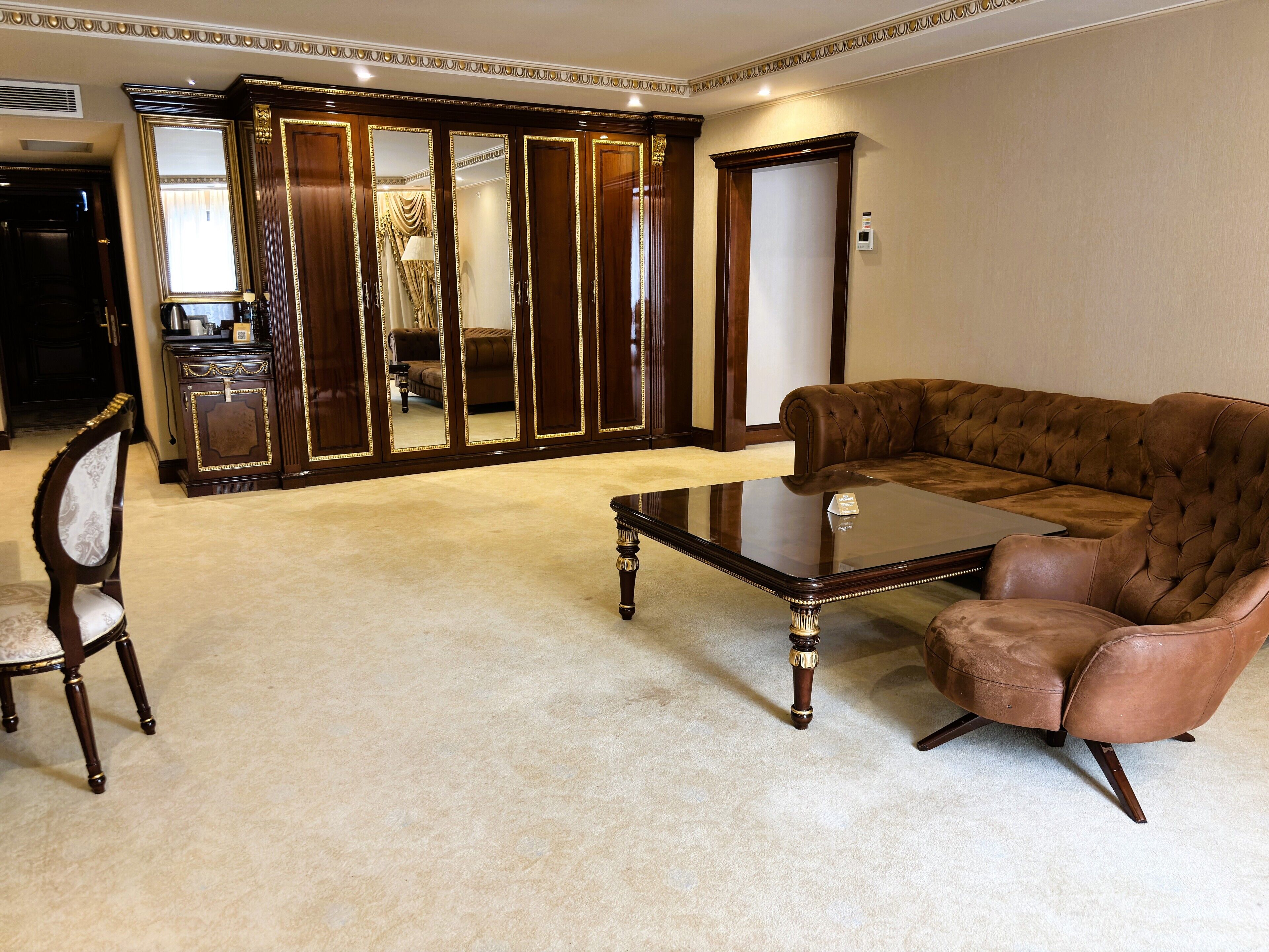 A spacious living room with a brown leather sofa, a wooden coffee table, and a large mirror with a decorative frame.