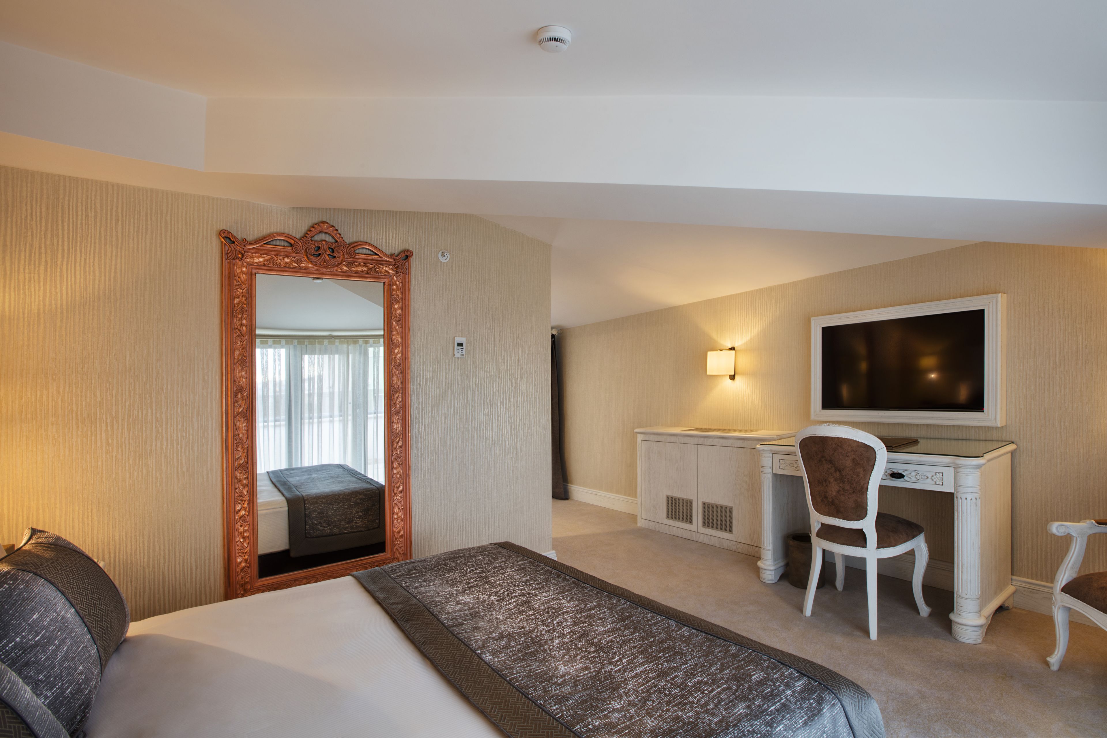 A hotel room with a large bed, a desk with a chair, a television, and a mirror.