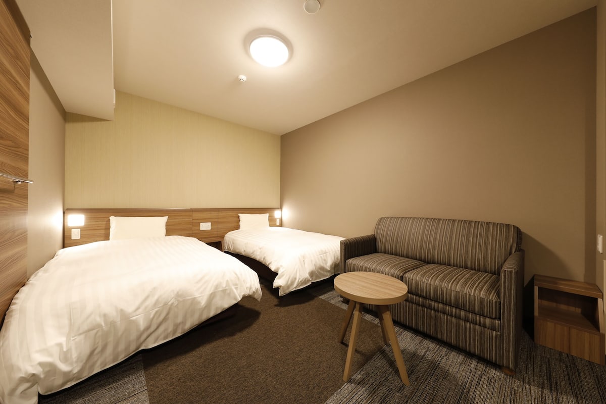 Habitación de hotel con dos camas, un sofá, una mesita y una lámpara de techo.