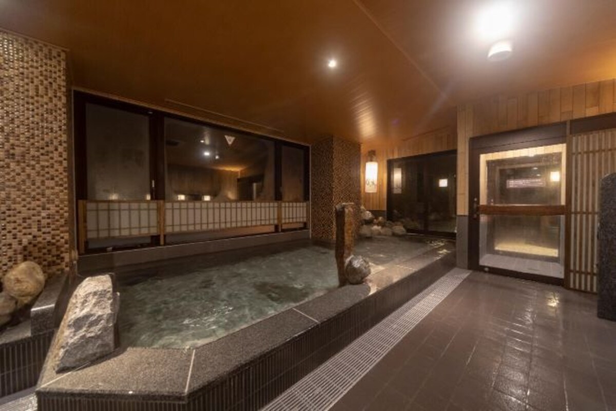 A traditional Japanese onsen with a stone bath, wooden walls, and a tiled floor.