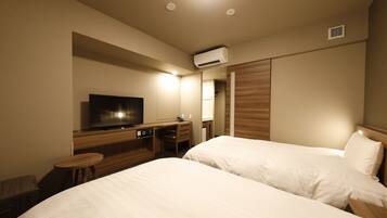 A hotel room with two beds, a desk with a television, and an air conditioning unit.