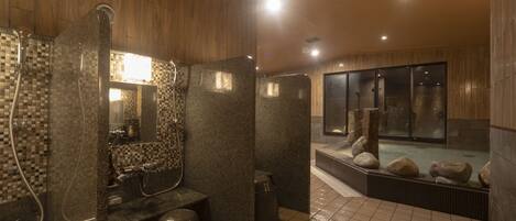 A modern bathroom with a shower, a sink, and a large mirror. There is a window and a stone wall.