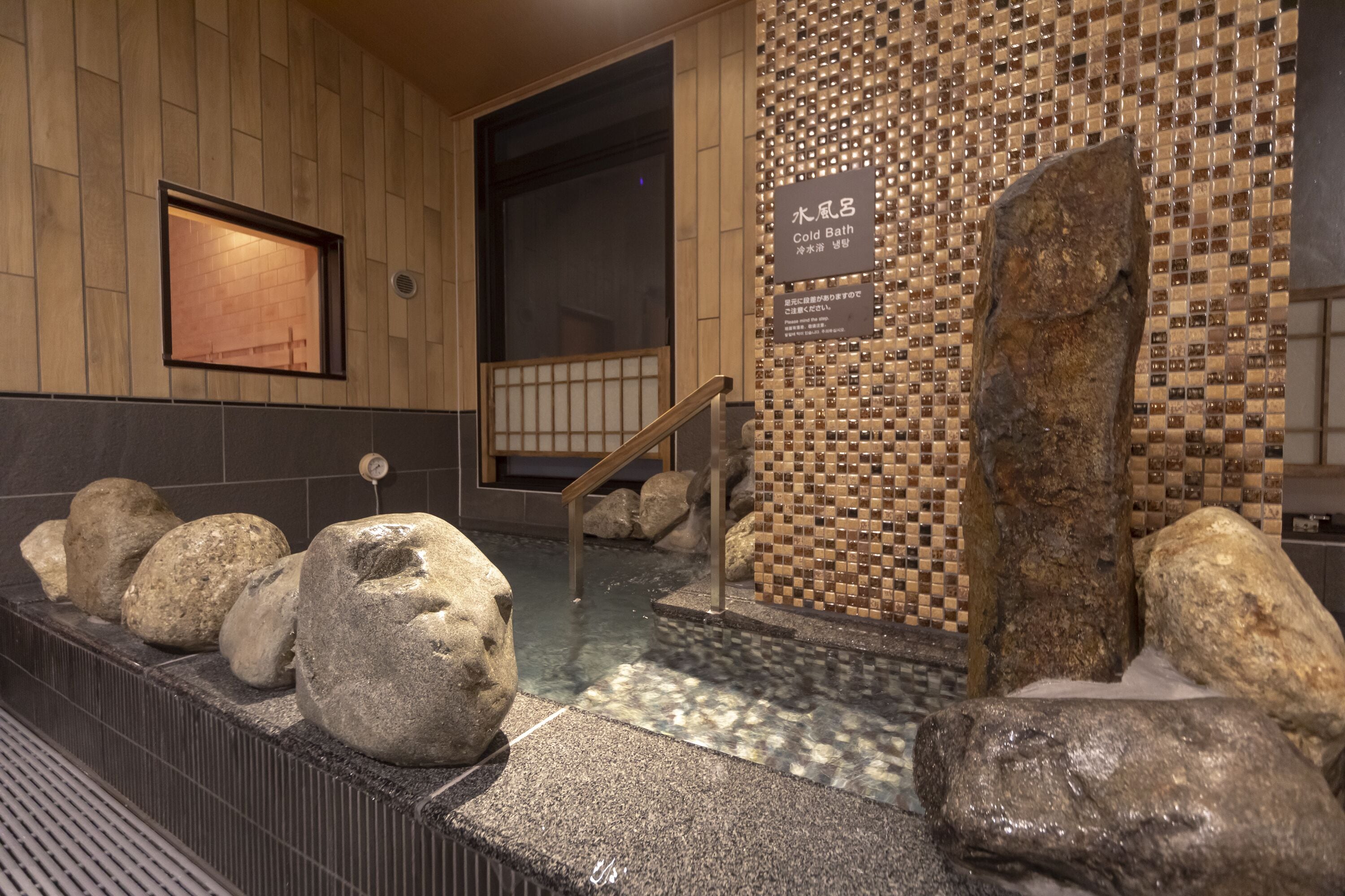 Un espace de baignade en pierre avec un mur en bois et un mur décoré d’une mosaïque de carreaux.