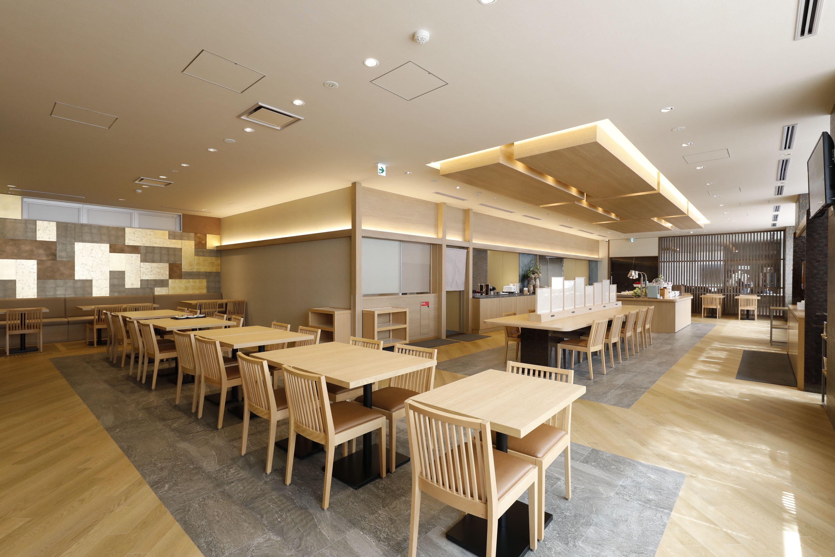 A spacious restaurant with wooden tables and chairs, a kitchen area, and a modern ceiling design.