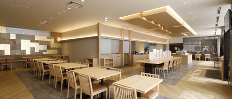 En rummelig restaurant med træborde og stole, et køkkenområde og et moderne loftdesign.