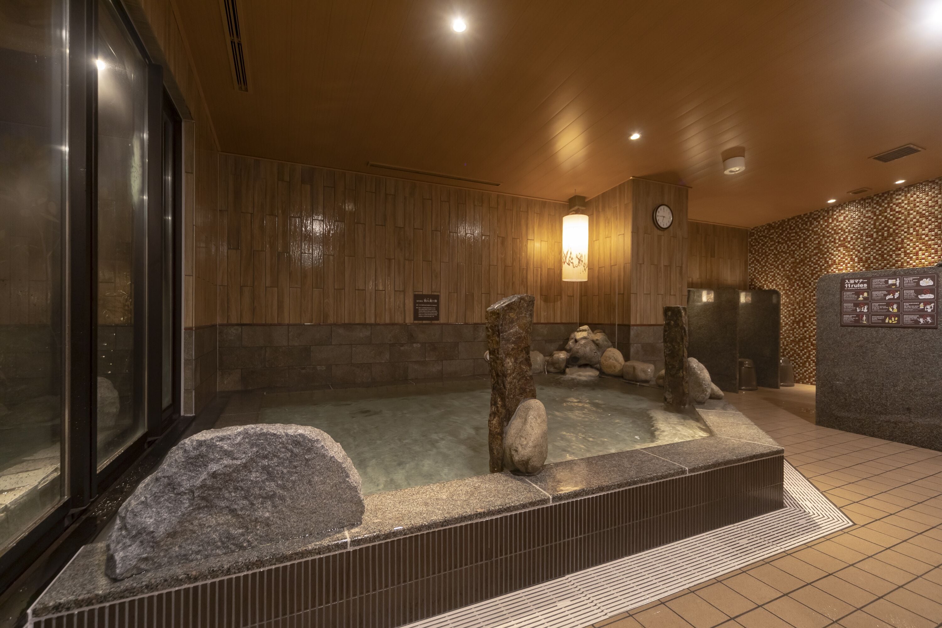 A traditional Japanese onsen with a stone bath surrounded by rocks and a wooden wall.