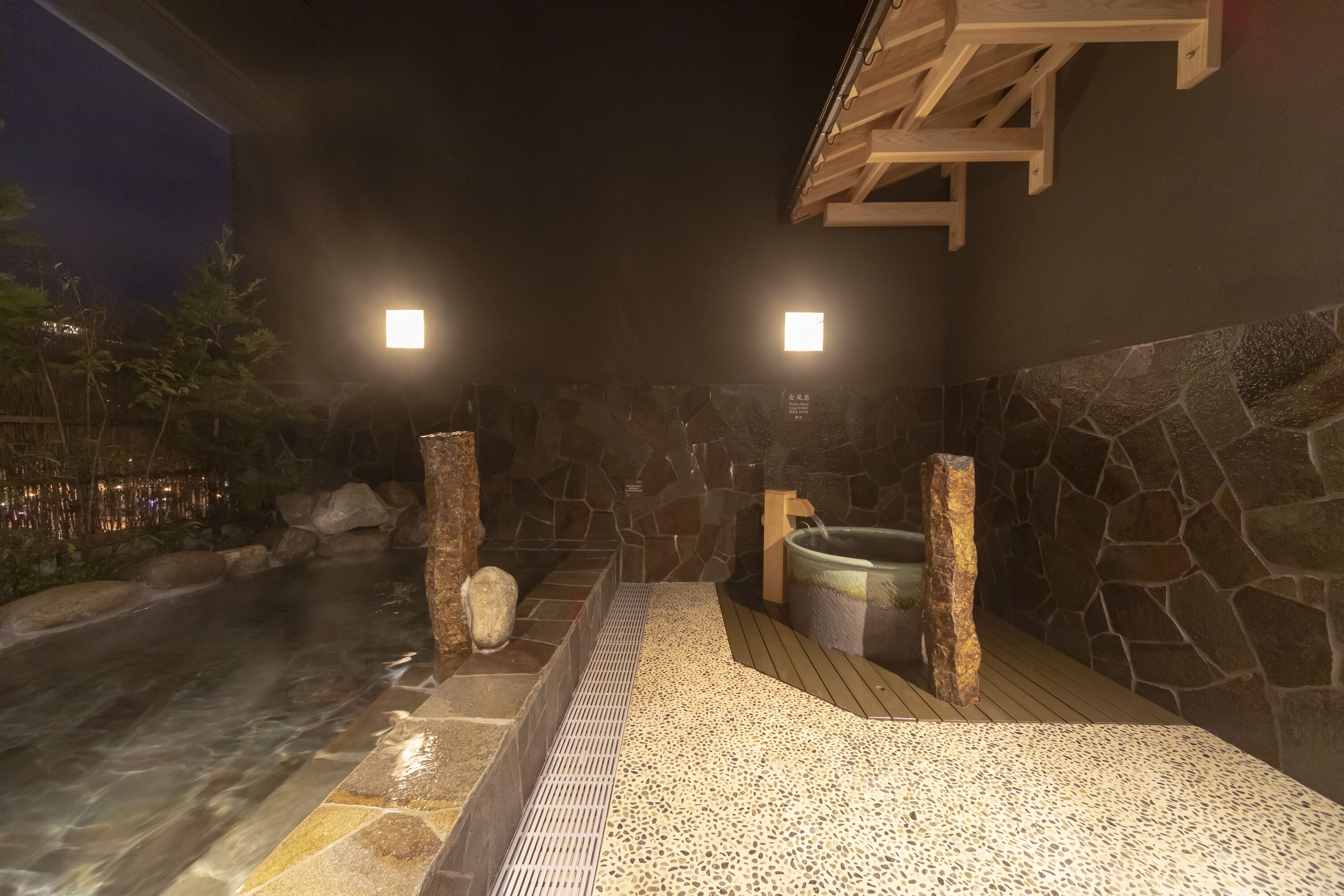 Un espace de sources chaudes doté de murs en pierre, d’une terrasse en bois et d’un bassin en pierre.