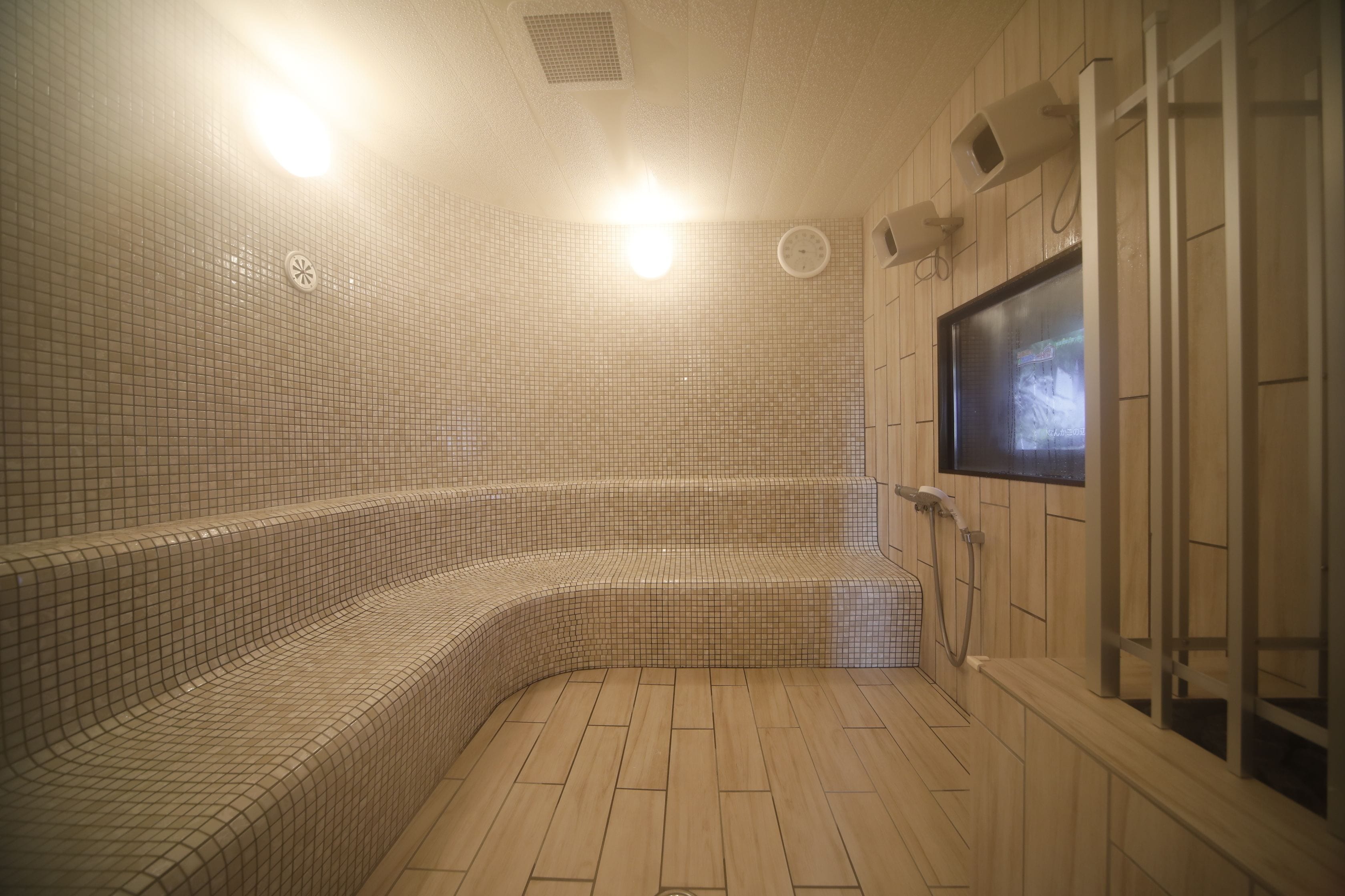 A sauna with tiled walls and wooden flooring, a television screen, and a shower area.