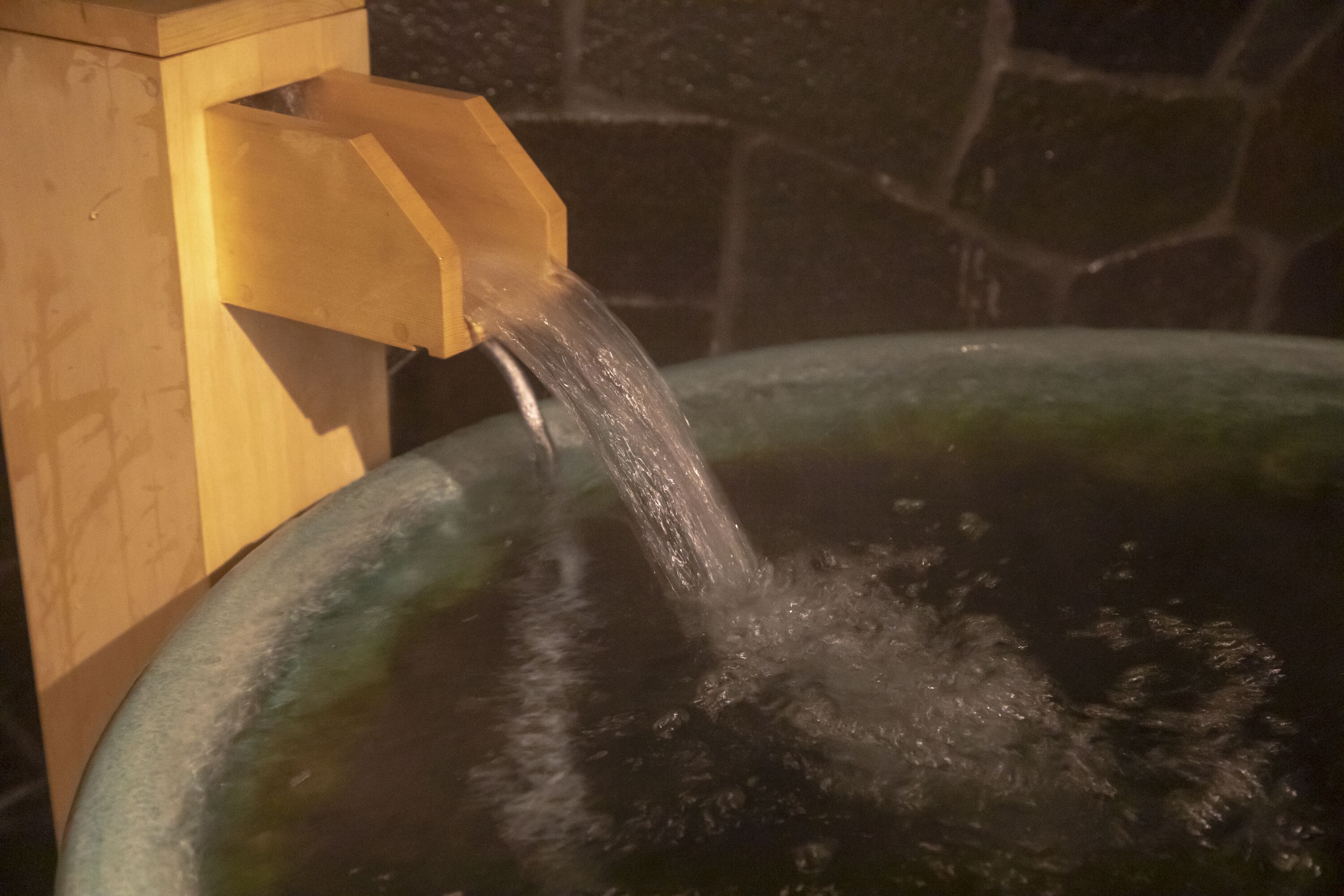 Eine Holzkonstruktion, in die Wasser in ein großes, rundes, grünliches Becken fließt.
