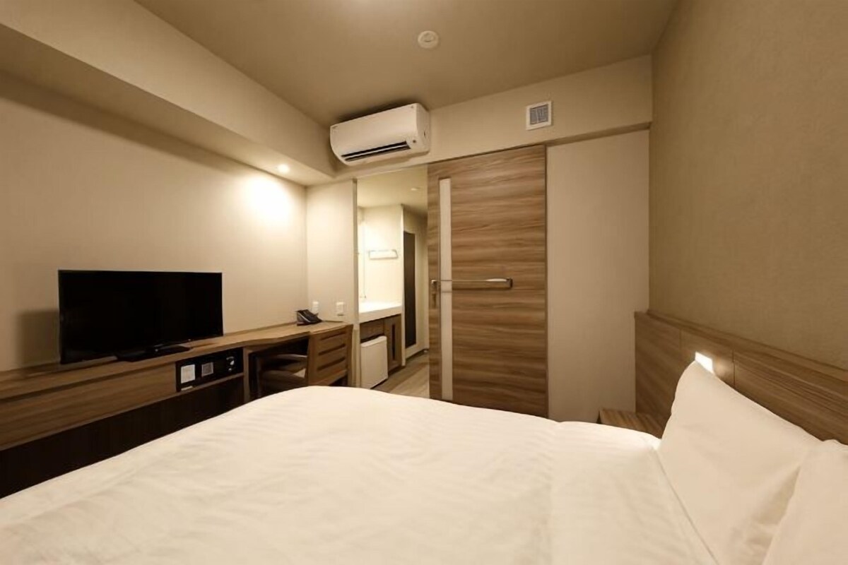 A hotel room with a bed, a TV, a desk, and a wardrobe.