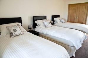 A room with three single beds, each with a headboard and a bedside table. There is a wooden wardrobe in the room. - Bamflatt Farm B&B (Strathaven)