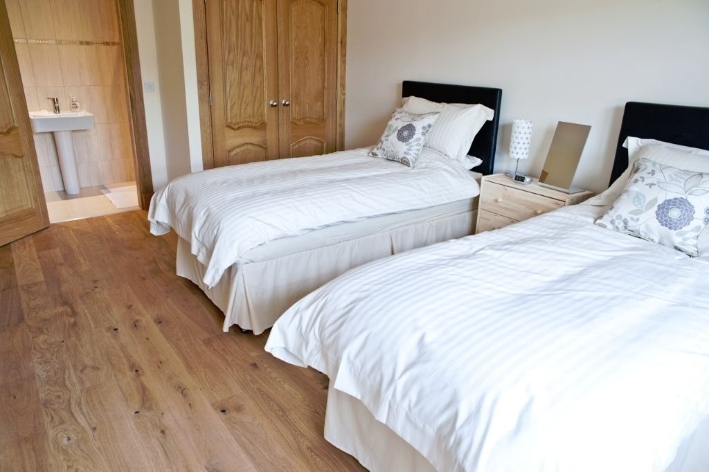 A bedroom with two beds, wooden flooring, a wooden wardrobe, and a bedside table with a lamp.