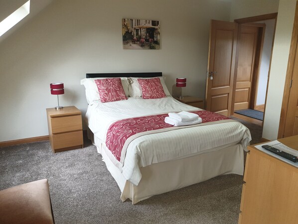 A neatly arranged bedroom with a bed, two bedside tables, a desk, and a door. - Bamflatt Farm B&B (Strathaven)