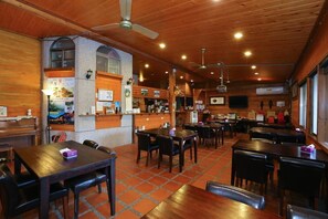 A restaurant with wooden interiors, multiple tables and chairs, and a bar area.