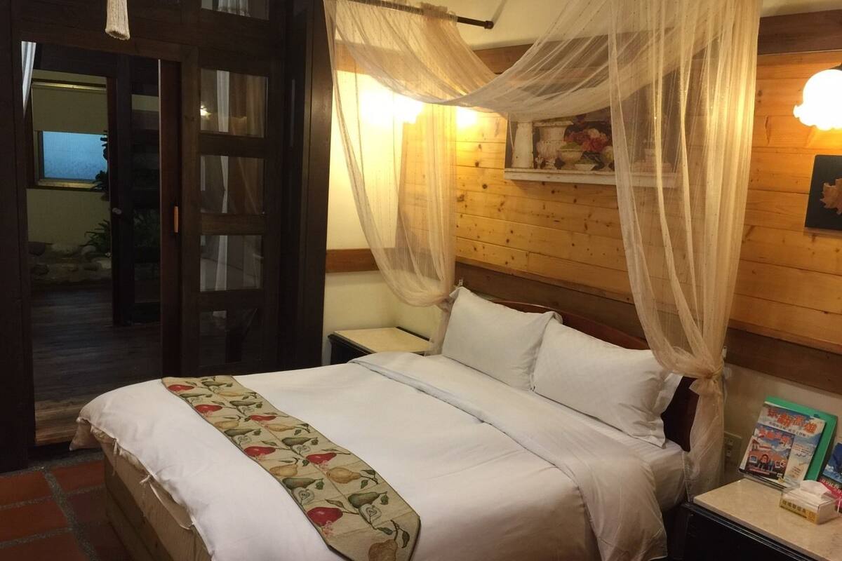 A bed with a canopy, a bedside table with a lamp, and a small shelf with a book.