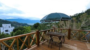 Eine Holzterrasse mit Tisch, Stühlen und Sonnenschirm, mit Blick auf eine gebirgige Landschaft.