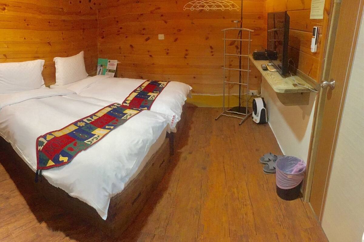 A wooden cabin room with a bed, a small table, a ladder, and a trash bin.
