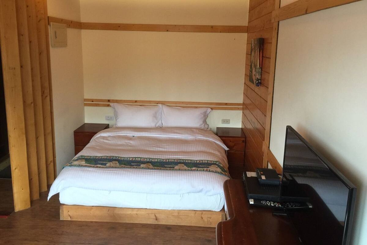 A bedroom with a wooden bed, a nightstand, a TV, and a wooden wall panel.
