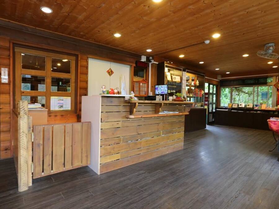 A wooden reception desk with a computer monitor, a refrigerator, and a small shelf with various items.
