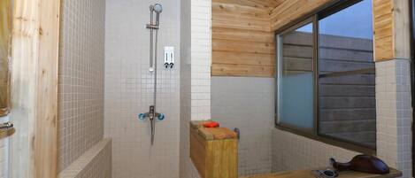 Un baño pequeño y cerrado con techo de madera y paredes de azulejos. Cuenta con una ducha con cabezal de ducha manual y un inodoro con asiento de madera.