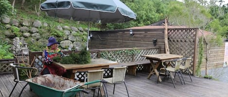 Un patio in legno con tavolo e sedie, un carriola e un ombrellone grande.