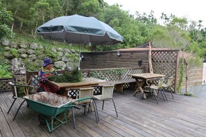 A wooden deck with a table and chairs, a wheelbarrow, and a large umbrella.