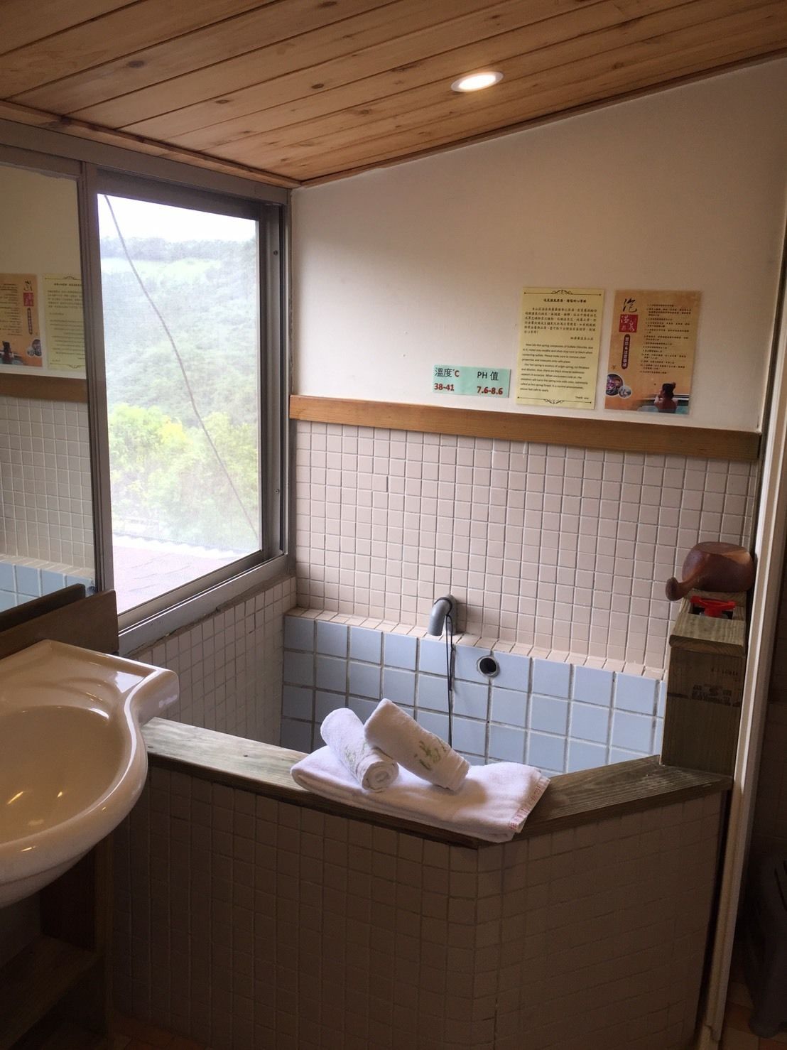 A bathroom with a sink, a window, and a shower area. There are towels on the counter and a sign with temperature and pH values.