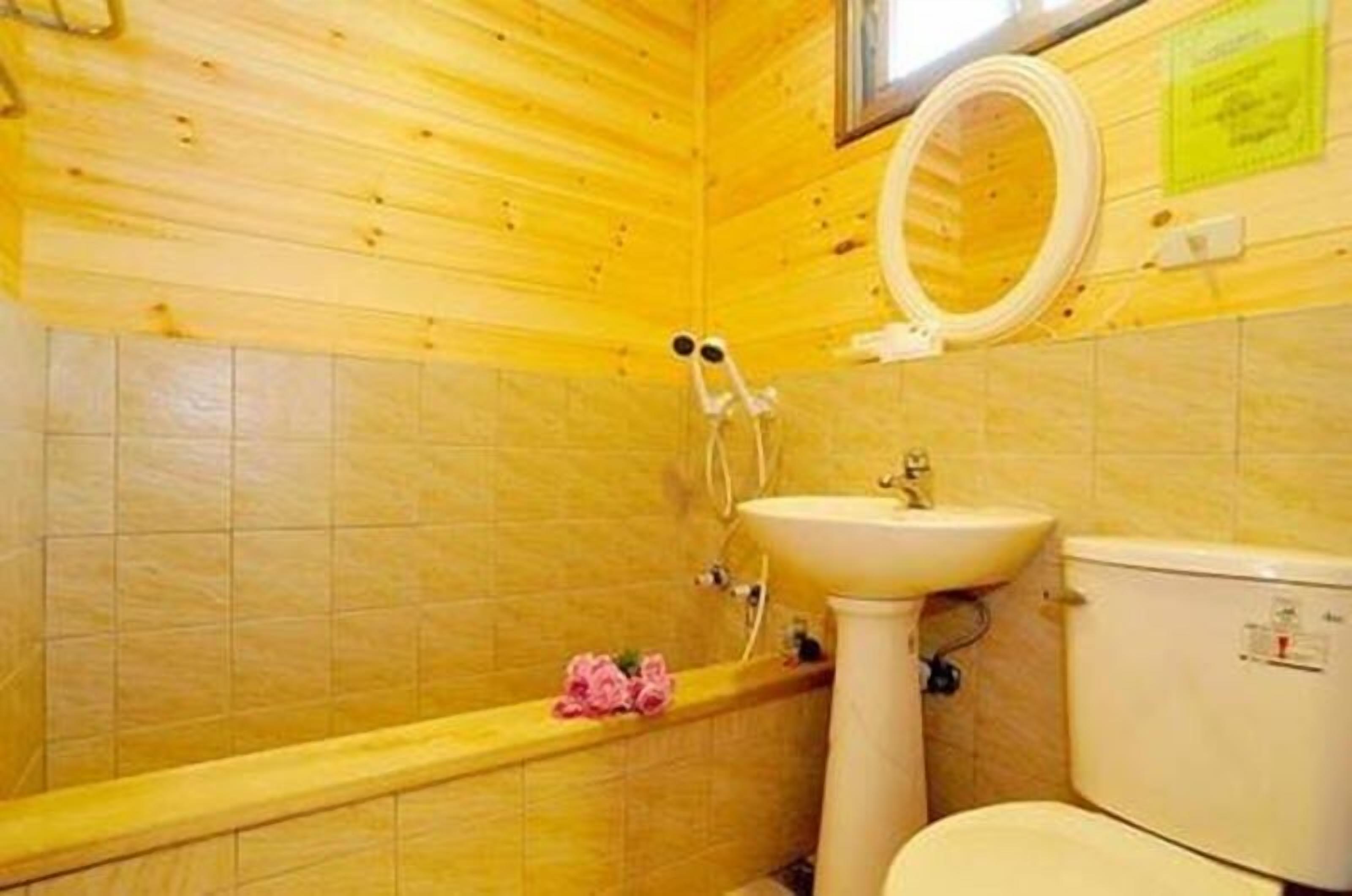 A bathroom with wooden walls, a white sink, a toilet, and a shower with a circular mirror.