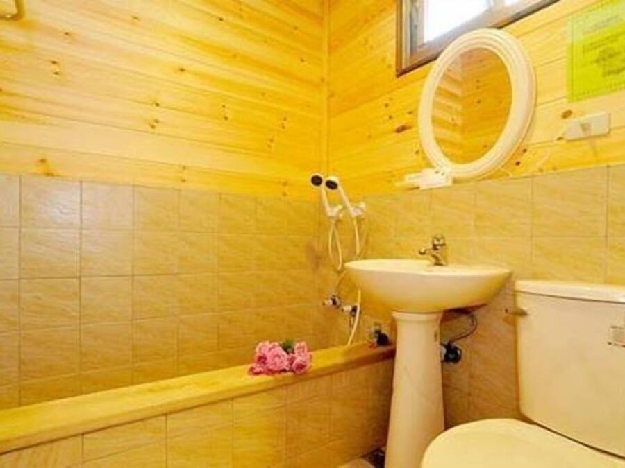 A bathroom with wooden walls, a white sink, a toilet, and a shower with a circular mirror.