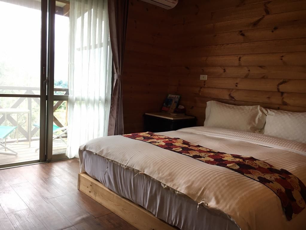 Een houten slaapkamer met een groot bed, een nachtkastje en uitzicht op de natuur door een schuifdeur.