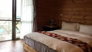Een houten slaapkamer met een groot bed, een nachtkastje en uitzicht op de natuur door een schuifdeur.